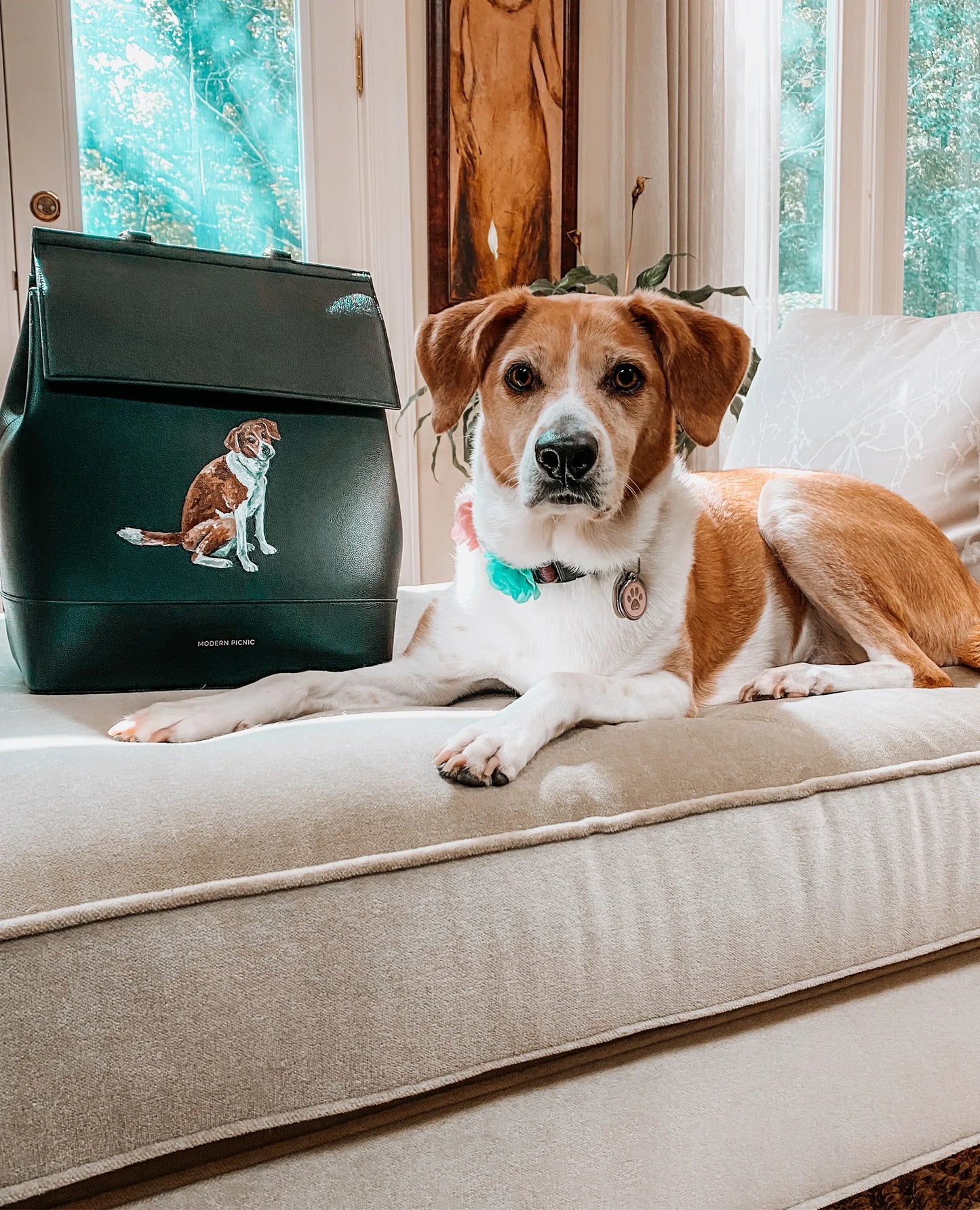 Dog laying on a couch next to the custom hand-painted Pet Portrait Snacker insulated pouch.