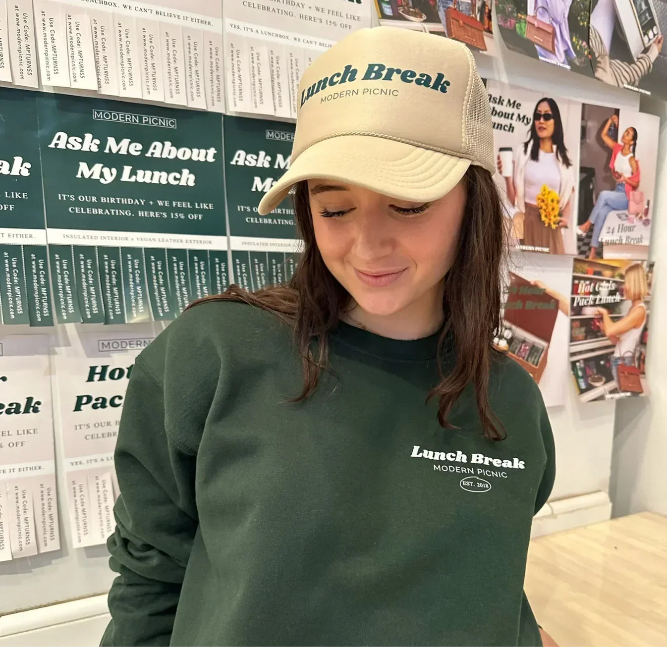 Woman wearing 'Lunch Break Modern Picnic' trucker hat and matching green sweatshirt, styled for work or casual outings.