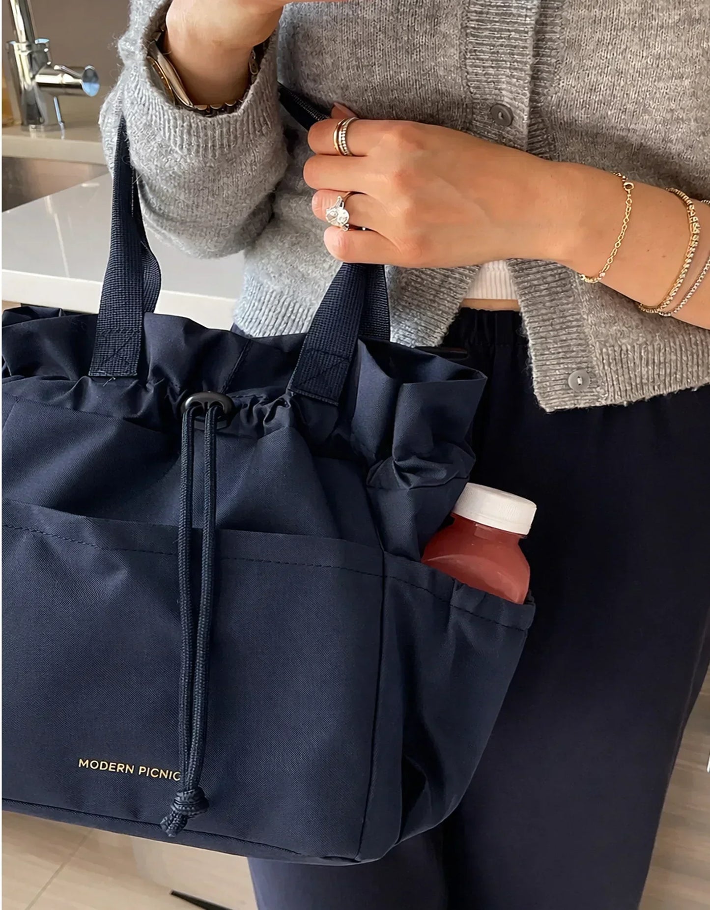 Navy blue insulated lunch tote with drawstring closure, holding a bottle, styled for work or travel.