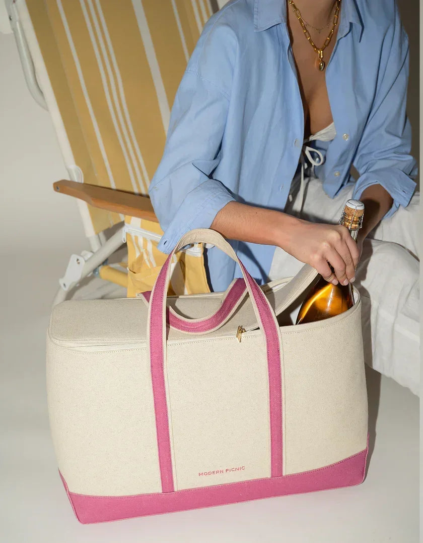 Cream canvas tote with pink straps holding champagne bottle, styled for chic outdoor picnics and travel