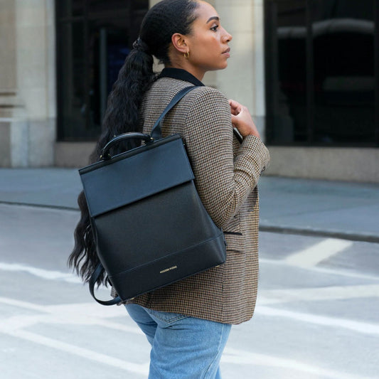 Woman wearing a black vegan leather insulated backpack in a city street setting