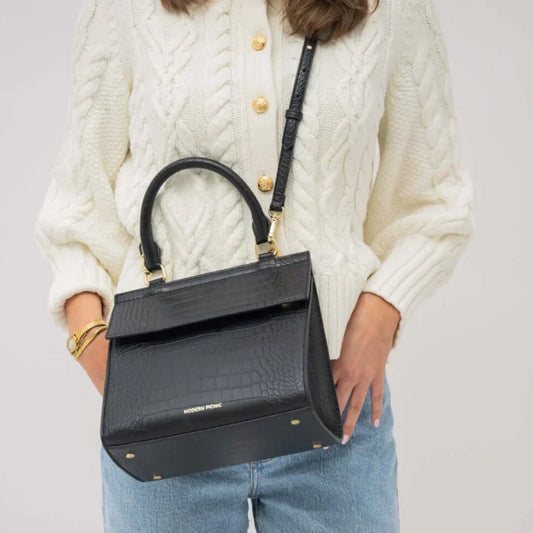 Woman wearing a cream sweater holding a black vegan leather lunch bag with gold accents