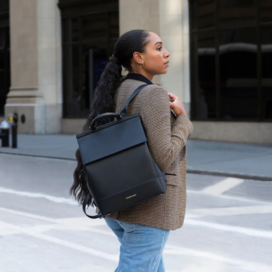 Woman carrying sleek black vegan leather backpack, stylish for work or travel, urban street setting