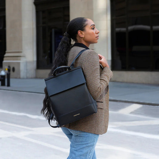 Woman carrying sleek black vegan leather backpack, stylish for work or travel, urban street setting