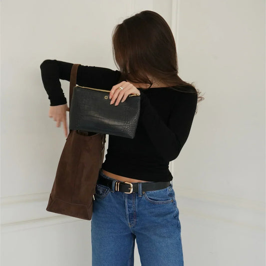 Woman holding black croc-texture clutch and brown suede tote, stylish everyday carry for work or travel