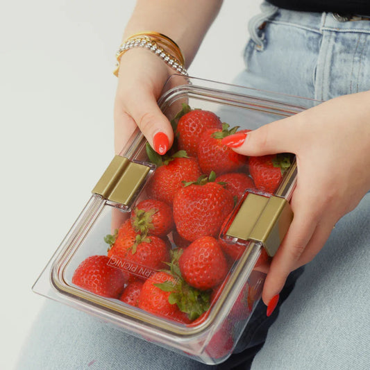 Woman holding a clear lunch container filled with fresh strawberries, healthy meal prep