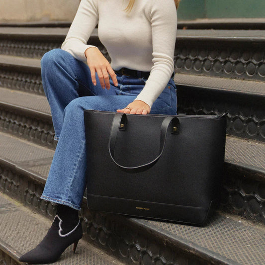 Woman sitting on outdoor steps with a large black vegan leather tote bag