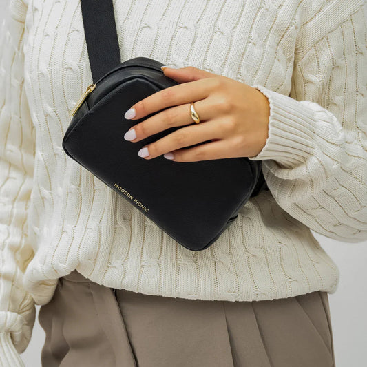 Woman wearing cream knit sweater and holding a black vegan leather crossbody bag