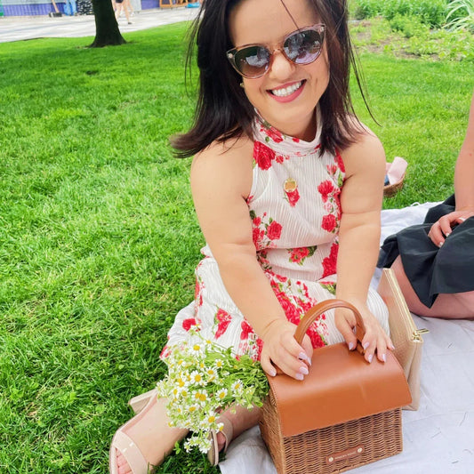 Woman in floral dress with sunglasses sitting on grass holding a chic insulated lunch bag
