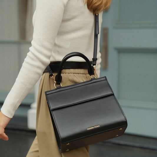 Stylish black vegan leather lunch tote with top handle and shoulder strap, perfect for work or travel.