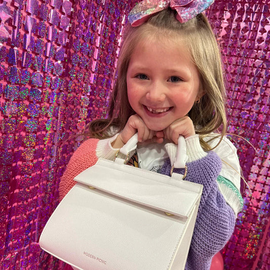 Smiling girl with sparkle bow holding white insulated lunch bag against pink sequin backdrop