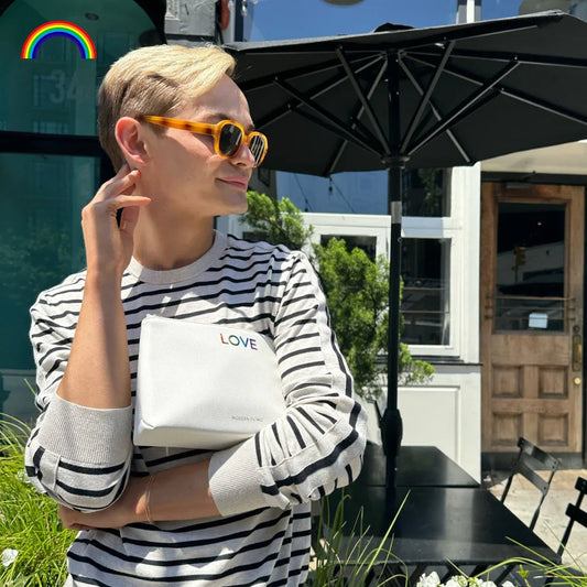 Man in striped shirt holding white 'LOVE' lunch bag outdoors under umbrella, stylish vegan leather tote for work or picnics