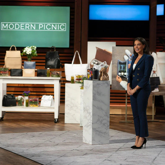 Woman presenting chic insulated lunch bags and totes on TV show set, display includes vegan leather bags and healthy food containers.