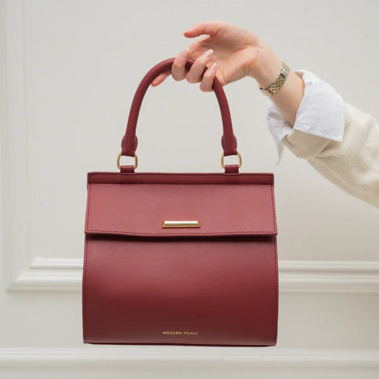 Hand holding a burgundy insulated vegan leather lunch bag with gold hardware