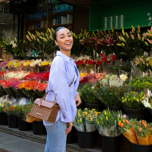 Woman smiling with woven vegan leather crossbody bag at flower market, stylish everyday tote for work or travel