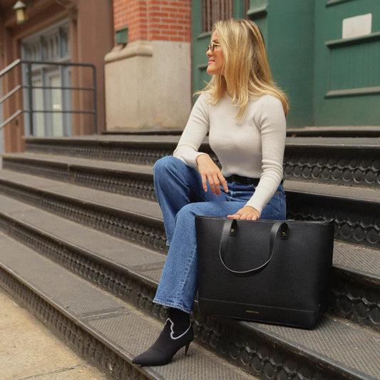 Woman sitting on steps with black vegan leather tote bag, stylish work accessory for everyday use