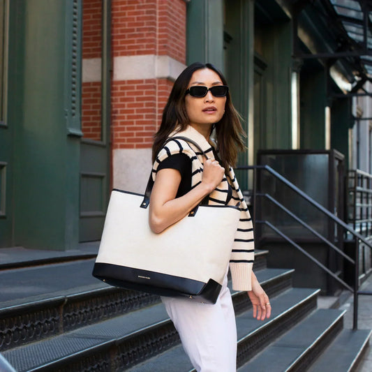 Woman carrying chic cream tote with black trim, stylish for work or travel, urban steps background