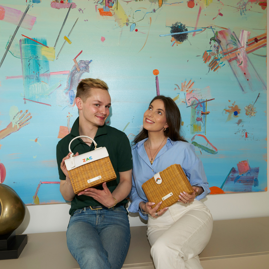 Two people holding vegan leather insulated lunch bags with basket weave design, sitting by a colorful abstract painting.