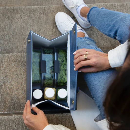 Stylish blue insulated lunch bag with compartments for salads and dressings, held by woman in jeans and white sneakers
