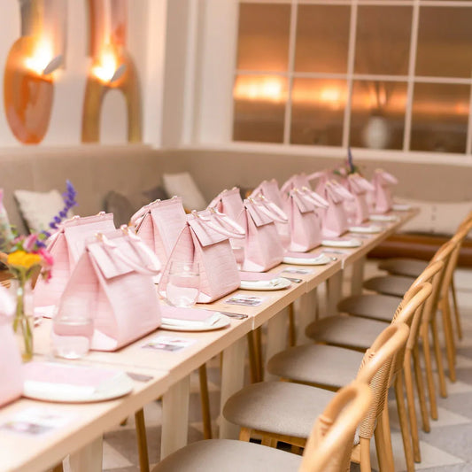 Pink vegan leather lunch bags on a long table, styled for a chic picnic or event with plates and flowers.