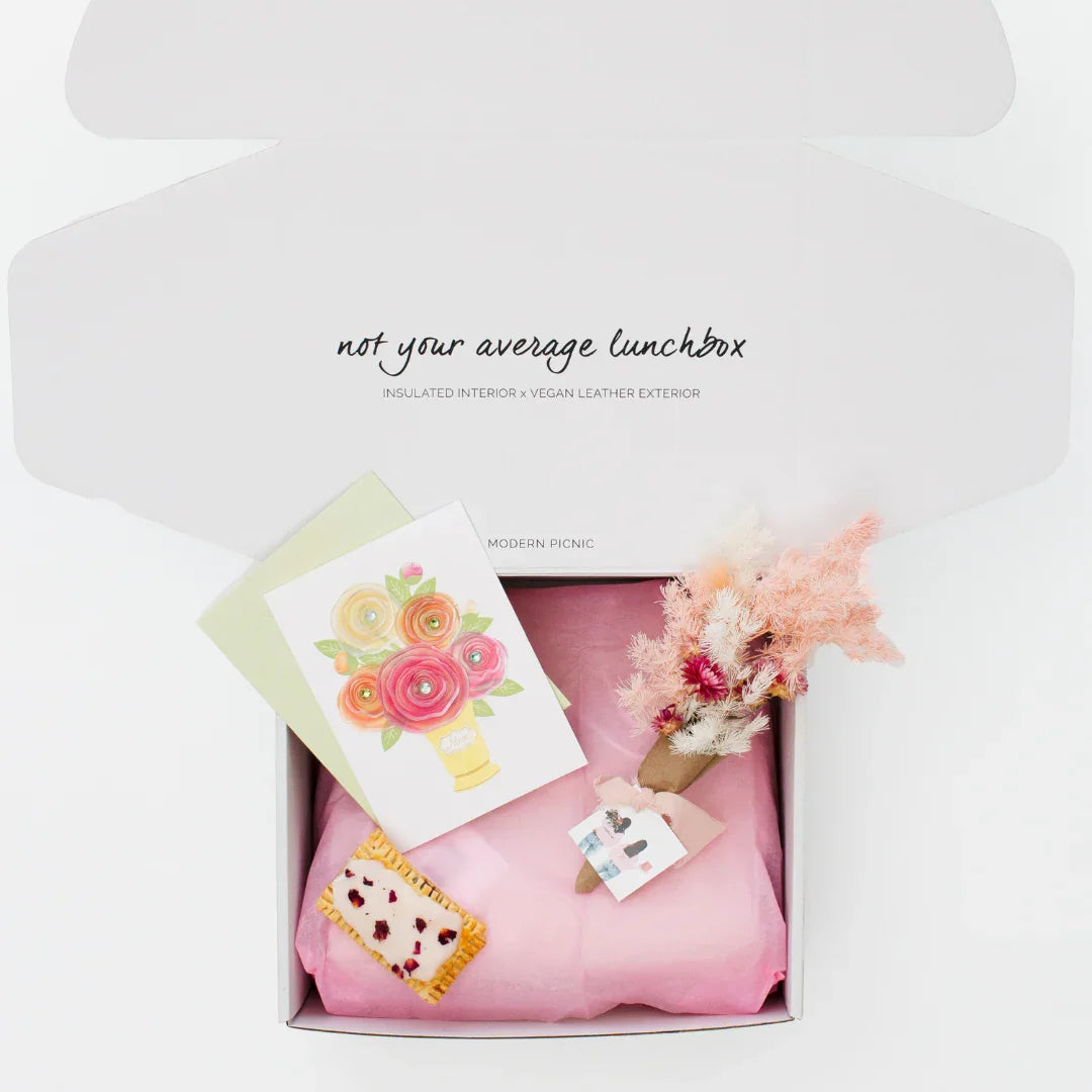 Stylish insulated lunchbox with vegan leather exterior, pink tissue, floral card, and dried flowers in gift box