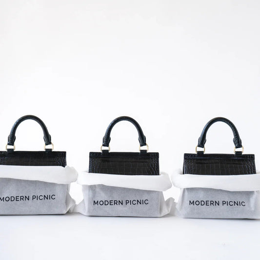 Three black croc-texture lunch bags with white insulation, branded 'MODERN PICNIC' on gray fabric base.