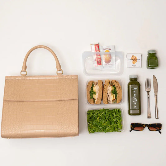 Beige croc-texture insulated lunch tote with healthy meal prep: sandwiches, greens, juice, snacks, and sunglasses.