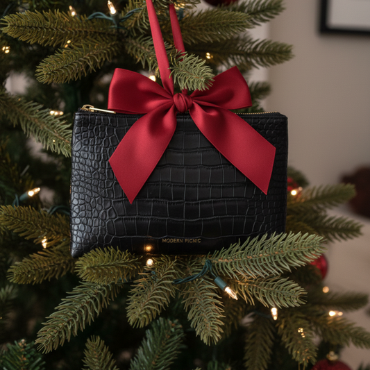 Black textured clutch with red bow hanging on Christmas tree, festive gift idea
