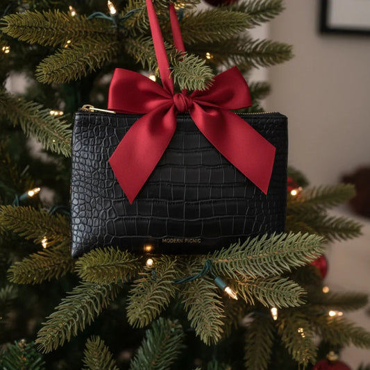 Black croc-texture vegan leather pouch with red bow, hanging on Christmas tree as holiday gift