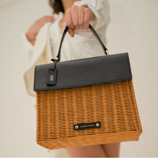 Woman holding a chic woven wicker lunch bag with black vegan leather flap and gold accents