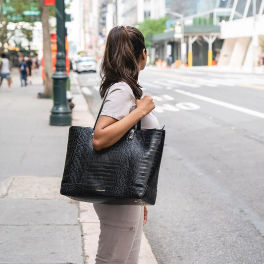 Woman carrying black croc-texture vegan leather tote bag on city sidewalk, stylish work accessory