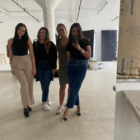 Four women in stylish outfits posing for a mirror selfie in a modern studio space