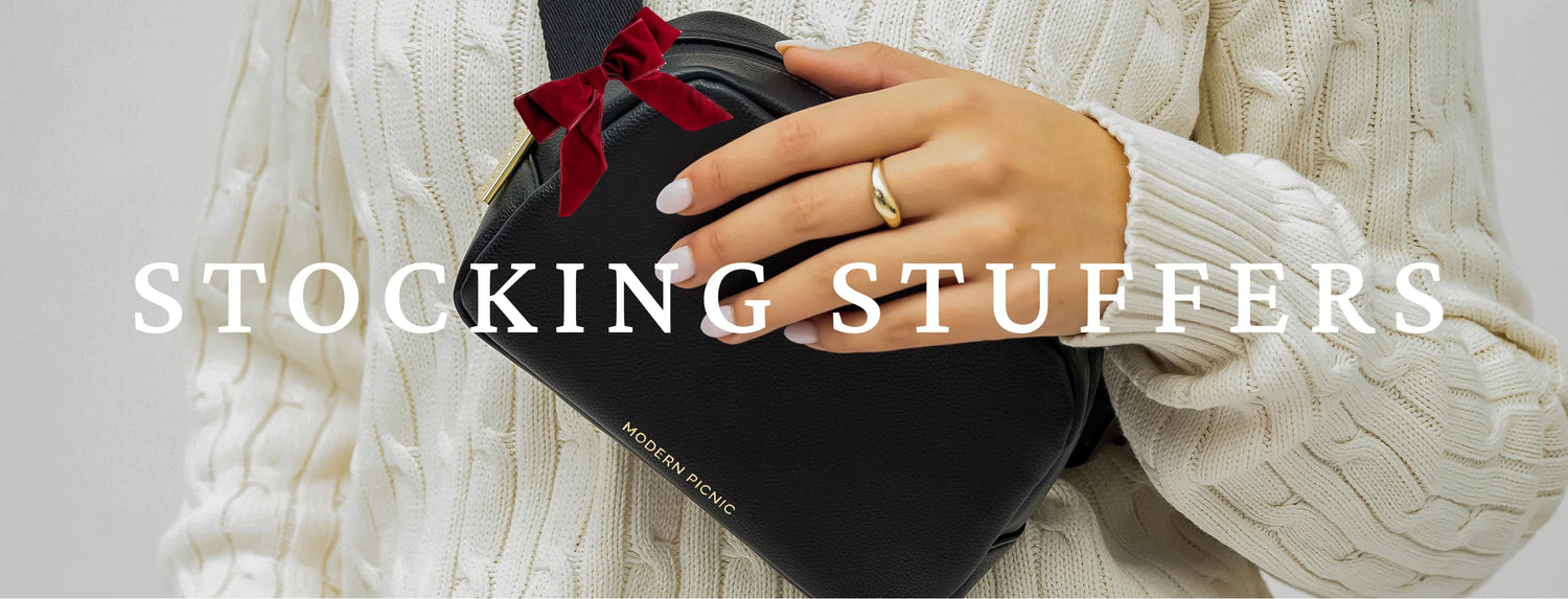 Woman in cream sweater holding black vegan leather lunch bag with red bow, holiday stocking stuffer