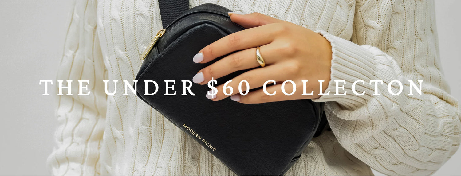 Woman in a cream sweater holding a black vegan leather crossbody lunch bag