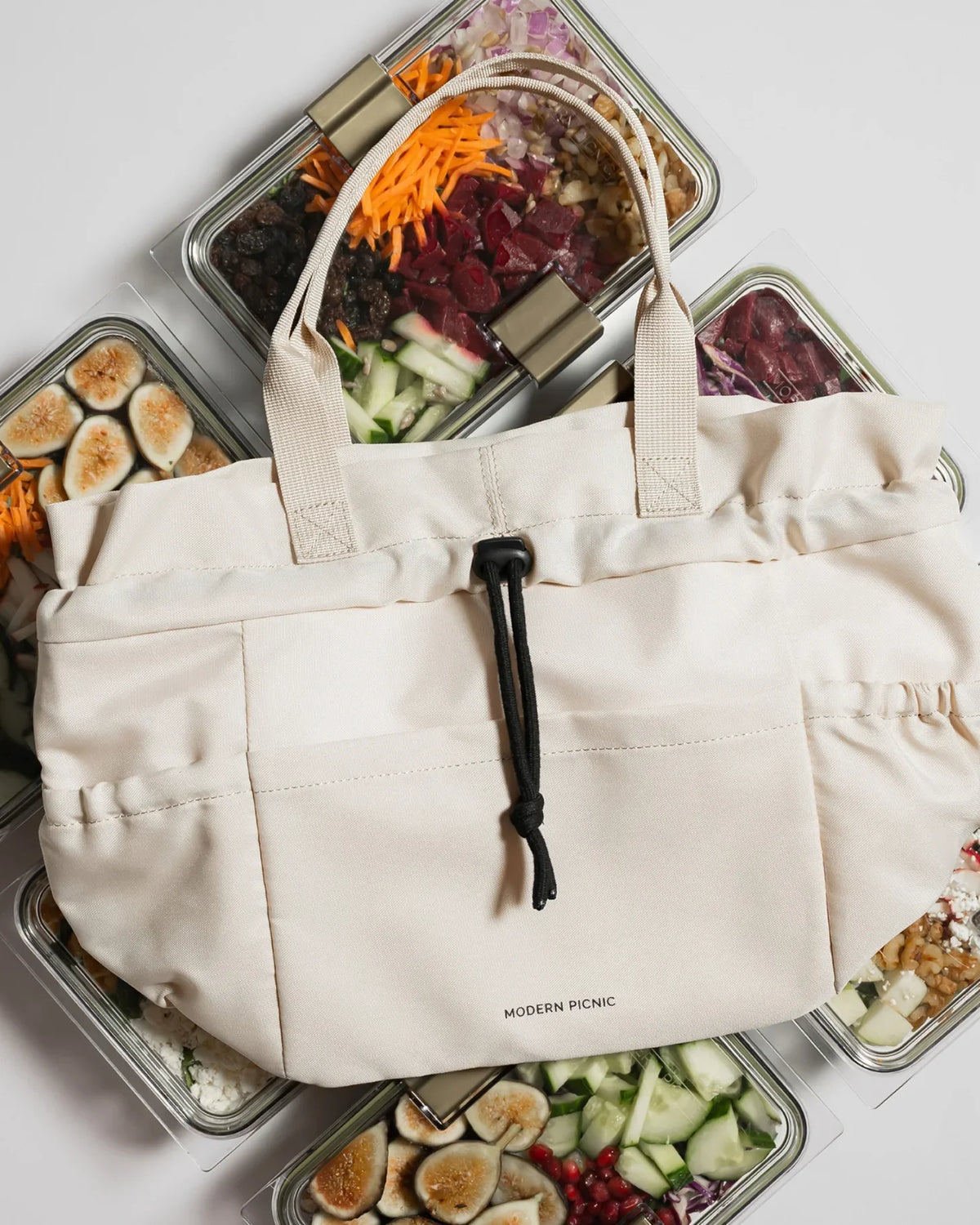 Cream insulated tote bag surrounded by healthy meal prep glass containers.