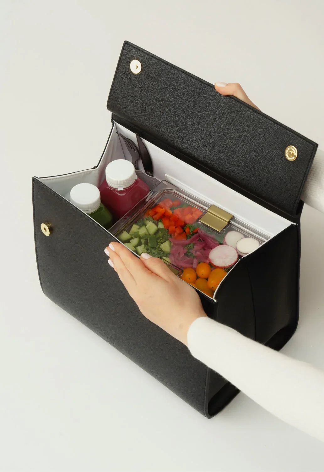 Black vegan leather lunch tote with insulated interior holding fresh salad, juice bottles, and utensils for healthy on-the-go meals.