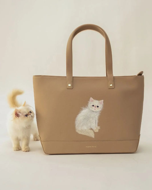 Tan vegan leather tote bag with white cat illustration, next to a real white fluffy cat
