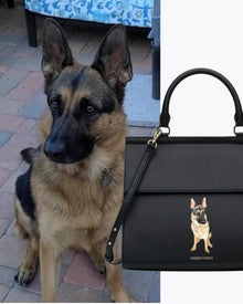 German Shepherd sitting outdoors next to a black vegan leather lunch bag with dog illustration