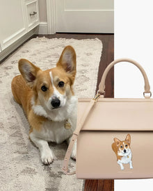 Corgi dog sitting on a rug beside a beige vegan leather lunch tote with dog illustration