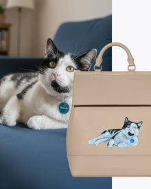 Beige insulated vegan leather lunch tote with embroidered black and white cat lying on blue couch.