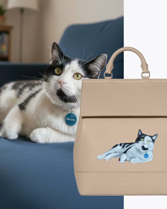 Beige insulated vegan leather lunch tote with embroidered black and white cat lying on blue couch.