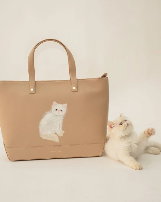 Beige vegan leather tote bag with white cat illustration next to fluffy white cat