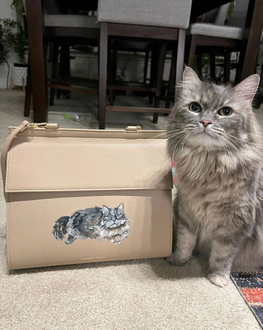 Gray long-haired cat beside tan vegan leather lunch bag with cat illustration