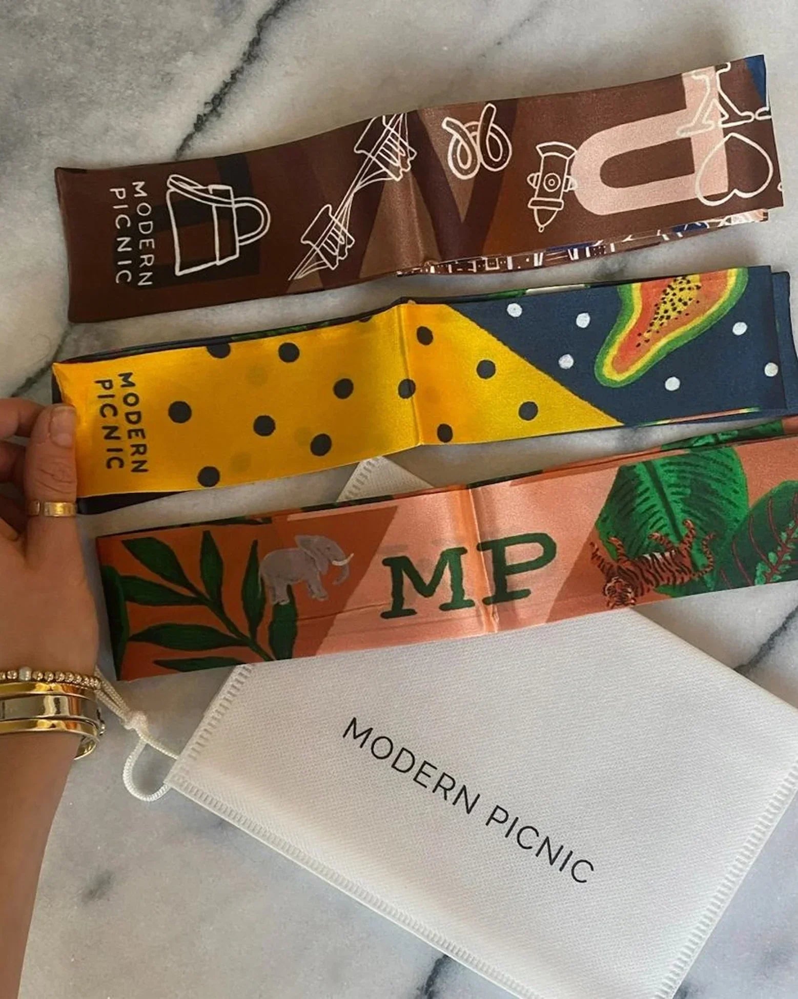 Colorful Modern Picnic branded scarves with playful patterns and designs, displayed on marble surface.