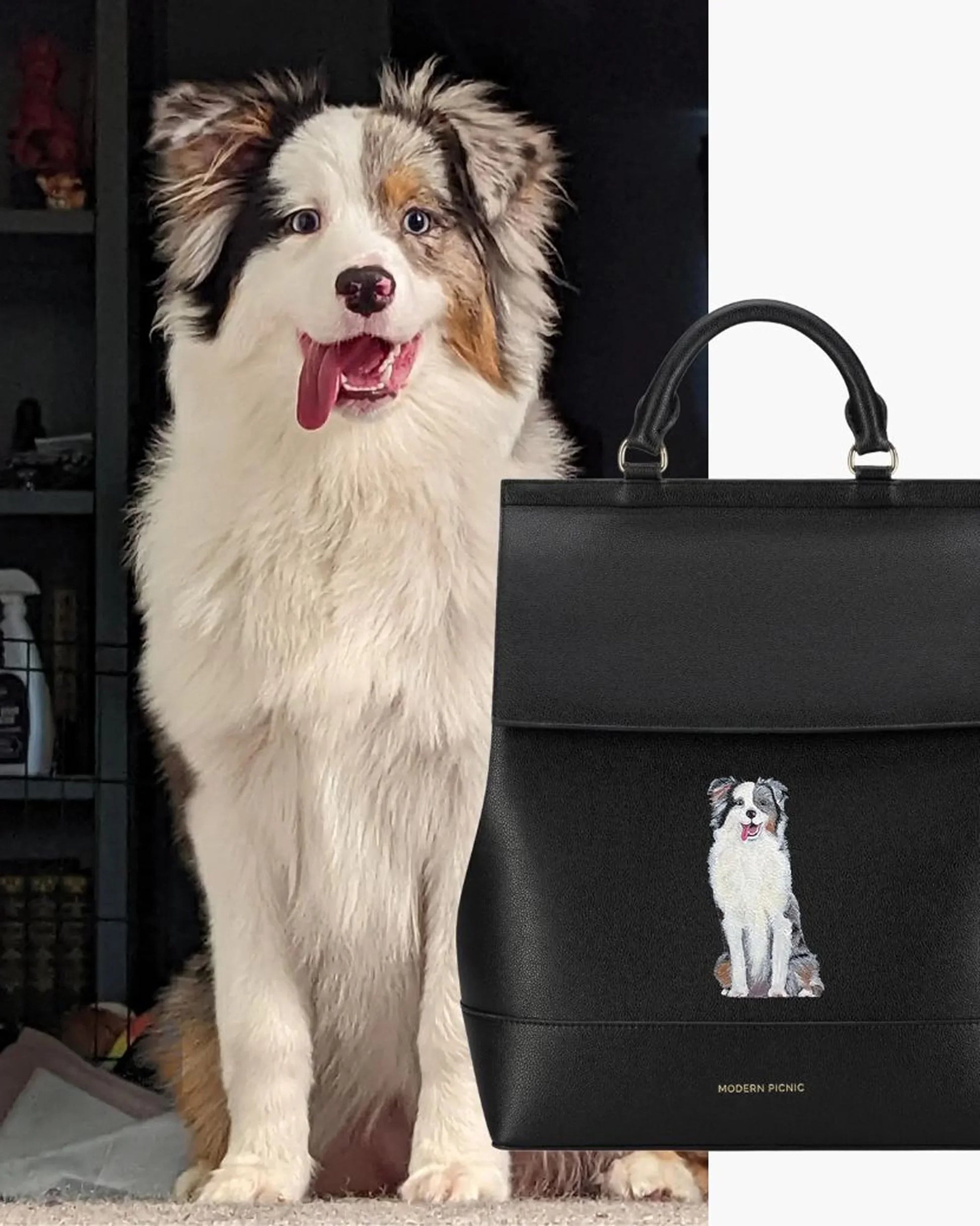 Fluffy dog sitting next to black vegan leather lunch tote with dog illustration and top handles