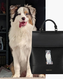 Fluffy dog sitting next to black vegan leather lunch tote with dog illustration and top handles