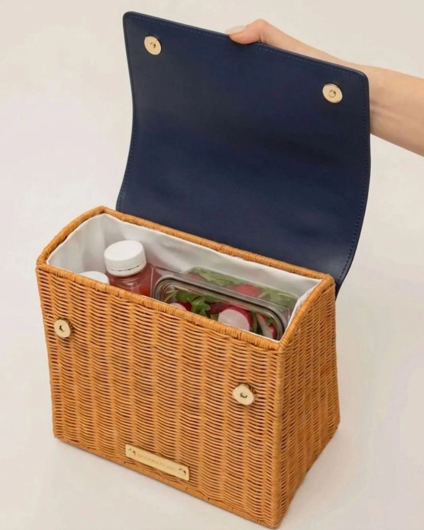 Woven picnic basket with navy lid, holding salad and drinks, ideal for stylish, insulated lunch storage.