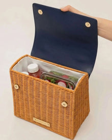 Woven picnic basket with navy lid, holding salad and drinks, ideal for stylish, insulated lunch storage.