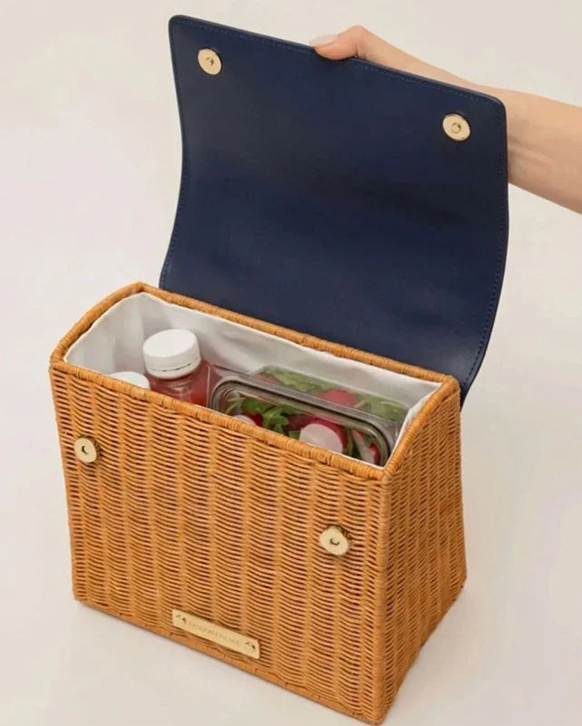 Woven picnic tote with navy lid, holding fresh salad and drinks, ideal for stylish lunches.