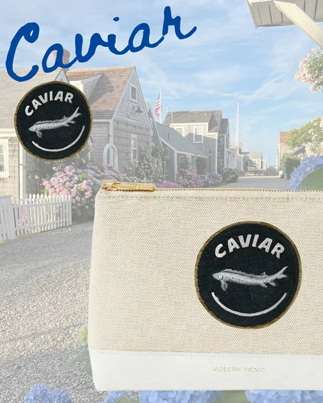 Cream canvas pouch with 'Caviar' fish patch, coastal backdrop — stylish lunch bag for work or travel